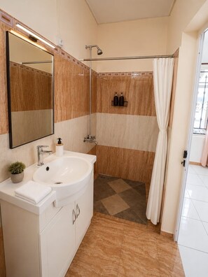 A bathroom with a large mirror, a sink, a shower, and a toilet. - Charming Apartment with a Pool in Grand Baie – Mauritius (Grand Baie)