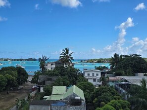 A coastal view with buildings, a clear sky, and boats in the water. - Charming Apartment with a Pool in Grand Baie – Mauritius (Grand Baie)