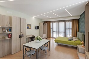 Una habitación de hotel moderna con cama, escritorio, silla, televisor y armario.
