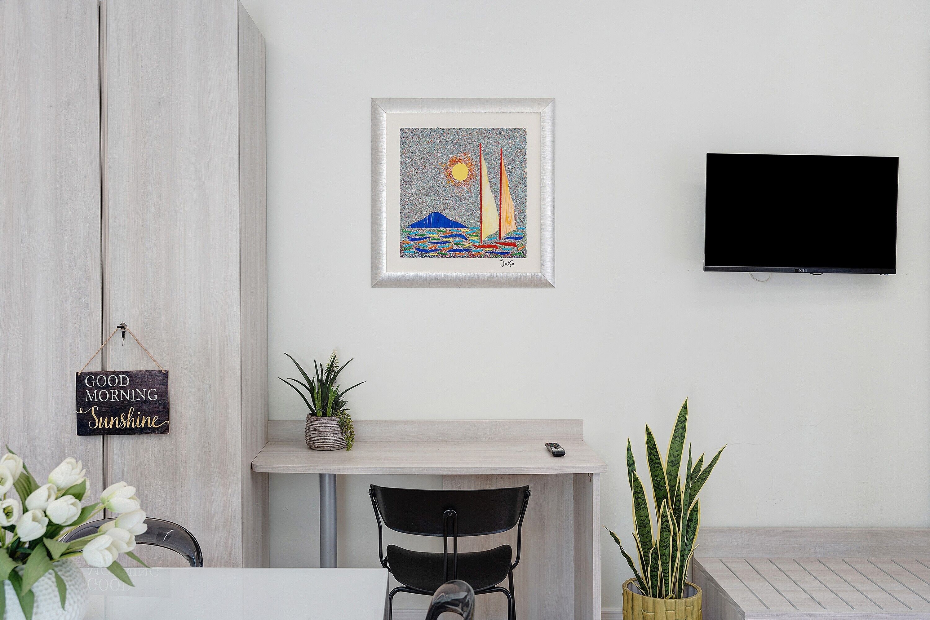 A modern living room with a mounted TV, a framed artwork, and a small table with a potted plant.
