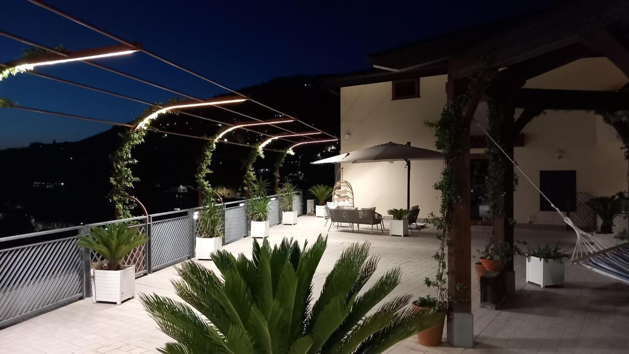 Un área de patio al aire libre con asientos, plantas en macetas y una estructura de pérgola.