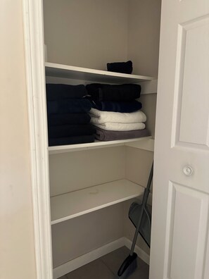 Ein Schrank mit Regalen, voll mit gefalteten Handtüchern, und ein Besen, der an der Wand lehnt.
