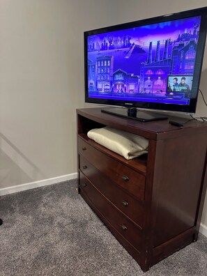 A television on a wooden cabinet with a remote control, a white towel, and a carpeted floor. - Cozy 1 BR /Uptown Lakes Area-/Your Minneapolis Home! Walk to everything! Dog OK! (Minneapolis)