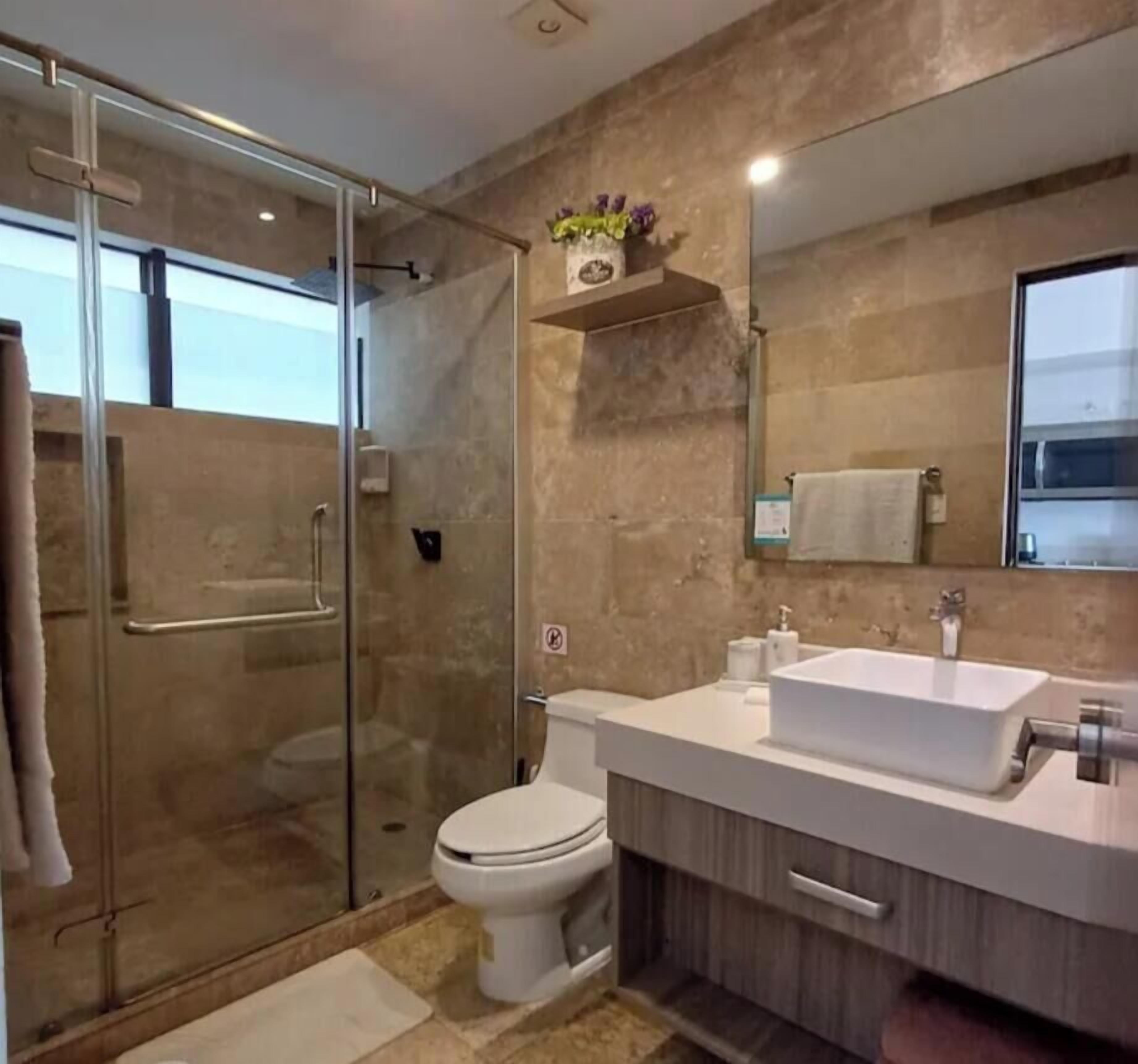 A modern bathroom with a glass shower enclosure, a white sink, and a large mirror.