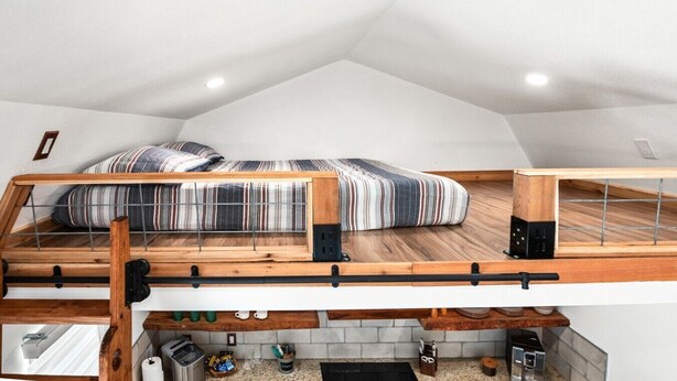 Una camera da letto mansardata con soffitto spiovente, un letto con biancheria a righe e un angolo cottura sottostante.
