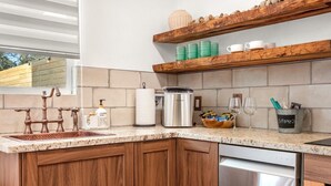Una cucina con un rubinetto in rame, un erogatore di detersivo per piatti, un porta asciugamani di carta, un bollitore in acciaio inossidabile, un cesto di snack e un portatazza con un'etichetta.