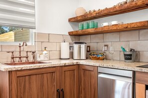 A kitchen with a copper faucet, a dish soap dispenser, a paper towel holder, a stainless steel kettle, a basket of snacks, and a mug holder with a label. - Secluded Couples Escape | Sauna + Plunge Pool (Wimberley)