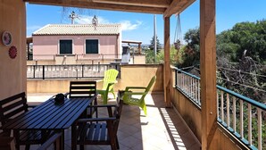 A covered outdoor area with a wooden table and chairs, a hanging light fixture, and a view of a building with a tiled roof. - The Residences 5 (Marina di Modica)