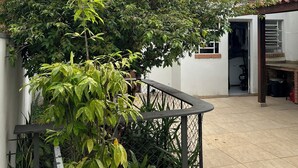 Ein Wohngebäude mit weißer Fassade, einem sichtbaren Klimagerät und einem eingezäunten Garten mit verschiedenen Pflanzen.