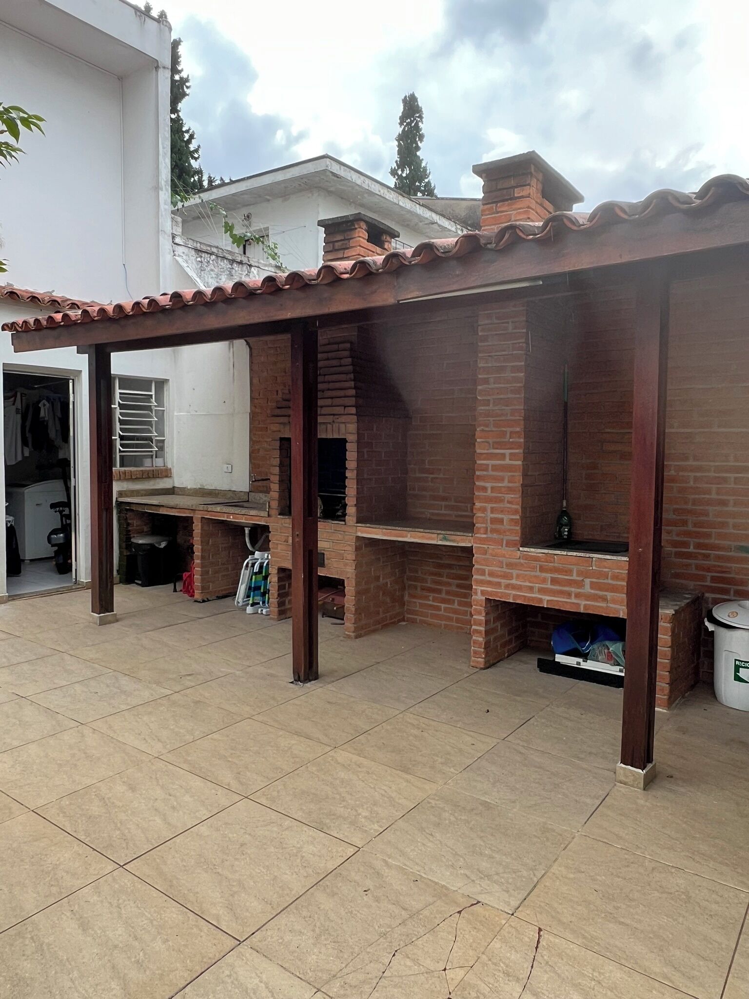 An outdoor patio with a brick barbecue area, a covered seating area, and a tiled floor.