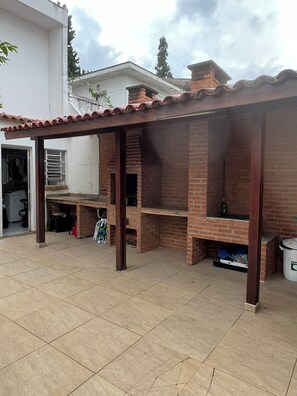 An outdoor patio with a brick barbecue area, a covered seating area, and a tiled floor.