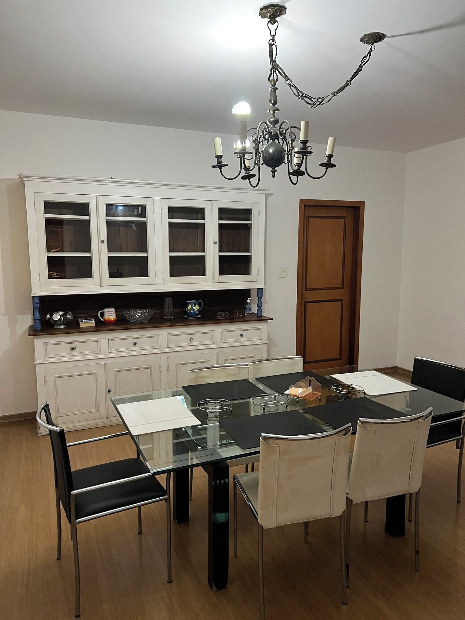 A dining area with a glass-top table, black chairs, and a white cabinet with glass doors.