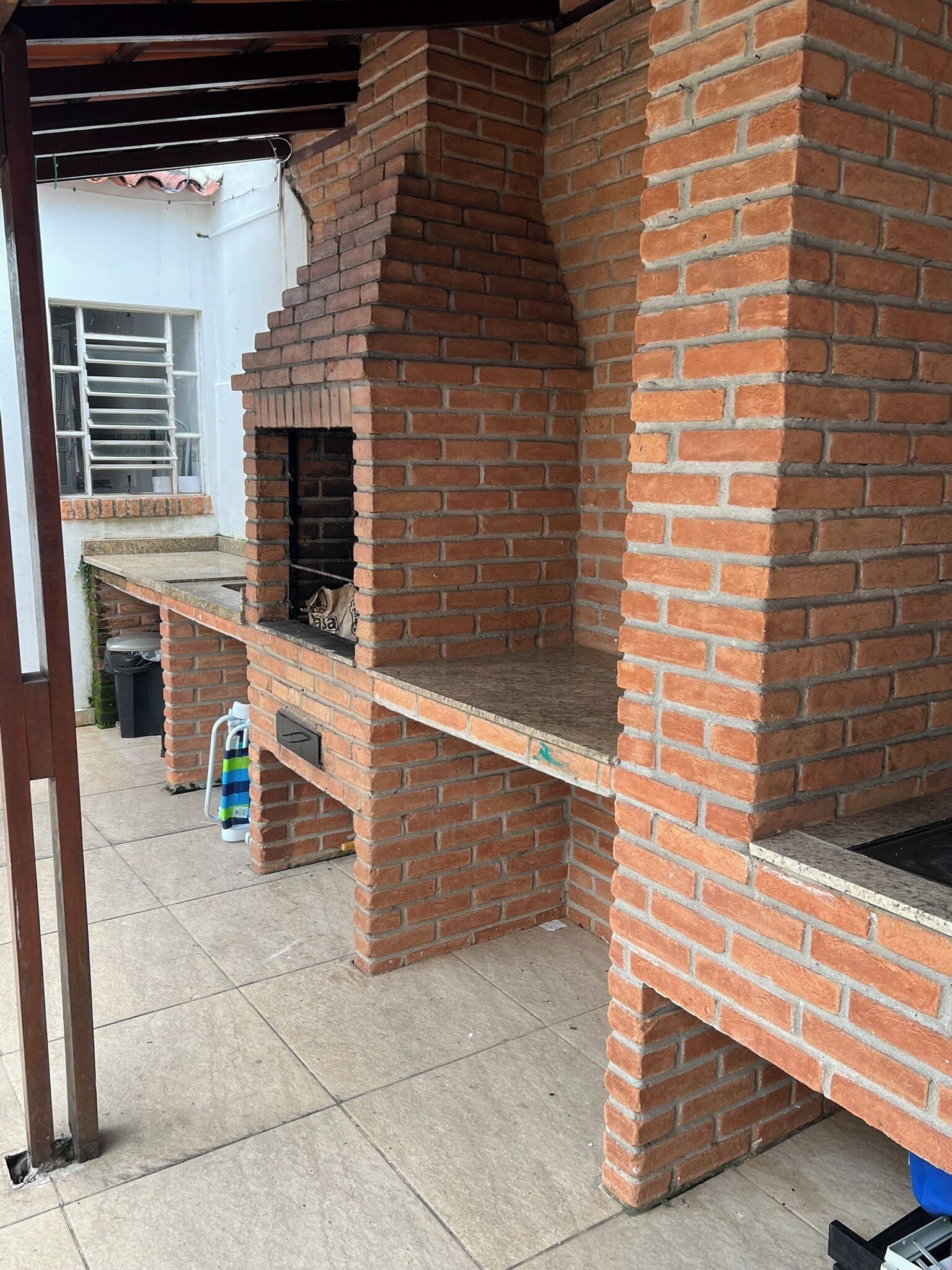 A brick-built outdoor barbecue area with a chimney, a tiled floor, and a metal grill.