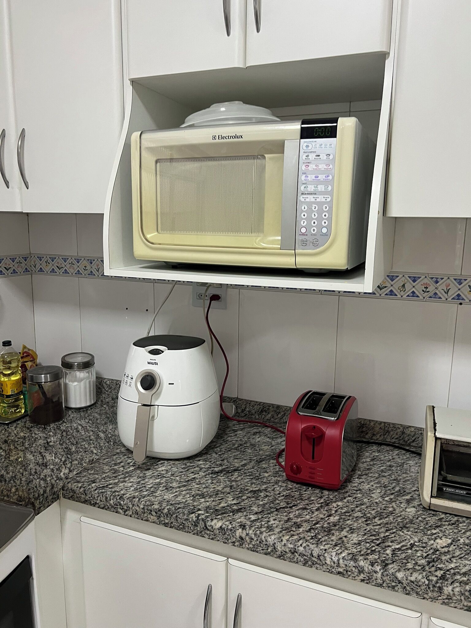 A kitchen with a microwave on a shelf, a toaster, and a rice cooker on the counter.