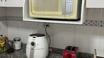 A kitchen with a microwave on a shelf, a toaster, and a rice cooker on the counter.