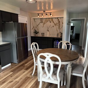 A modern kitchen with a built-in refrigerator, a dining area with a wooden table and white chairs, and a marble backsplash.