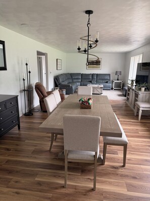 A spacious living area with a large sectional sofa, a dining table with chairs, and a chandelier.