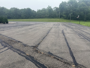 A large, empty parking lot with visible cracks and patches of grass.