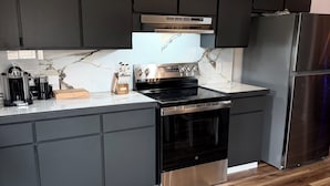 A modern kitchen with dark cabinets, a stainless steel refrigerator, and a marble backsplash.