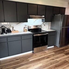 A modern kitchen with dark cabinets, a stainless steel refrigerator, and a marble backsplash.