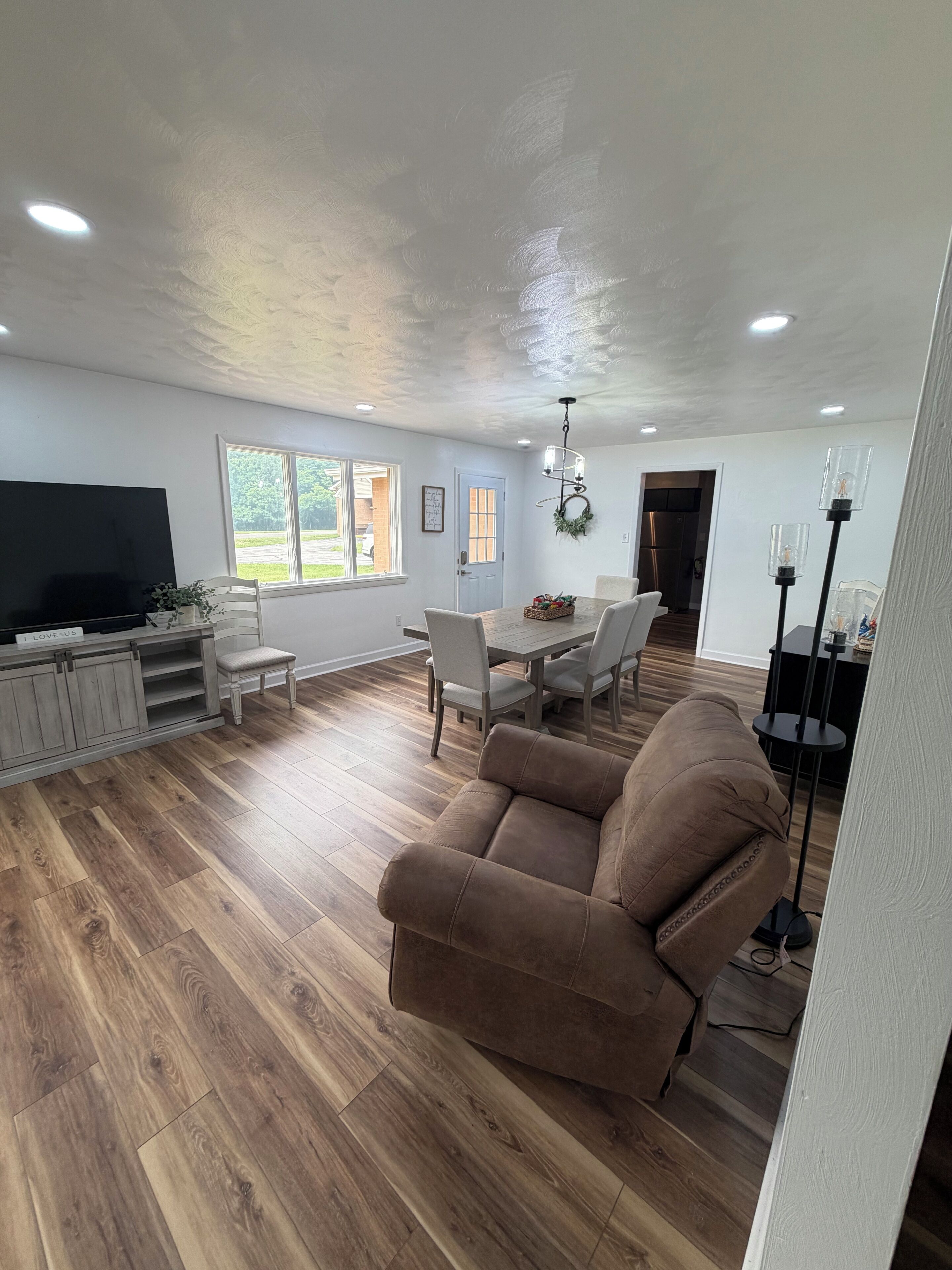 Un salón amplio con una televisión de pantalla plana, piso de madera, un sofá marrón y un comedor con mesa y sillas.
