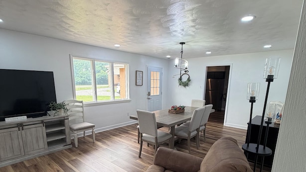A spacious living room with a flat-screen TV, wooden flooring, a brown sofa, and a dining area with a table and chairs.