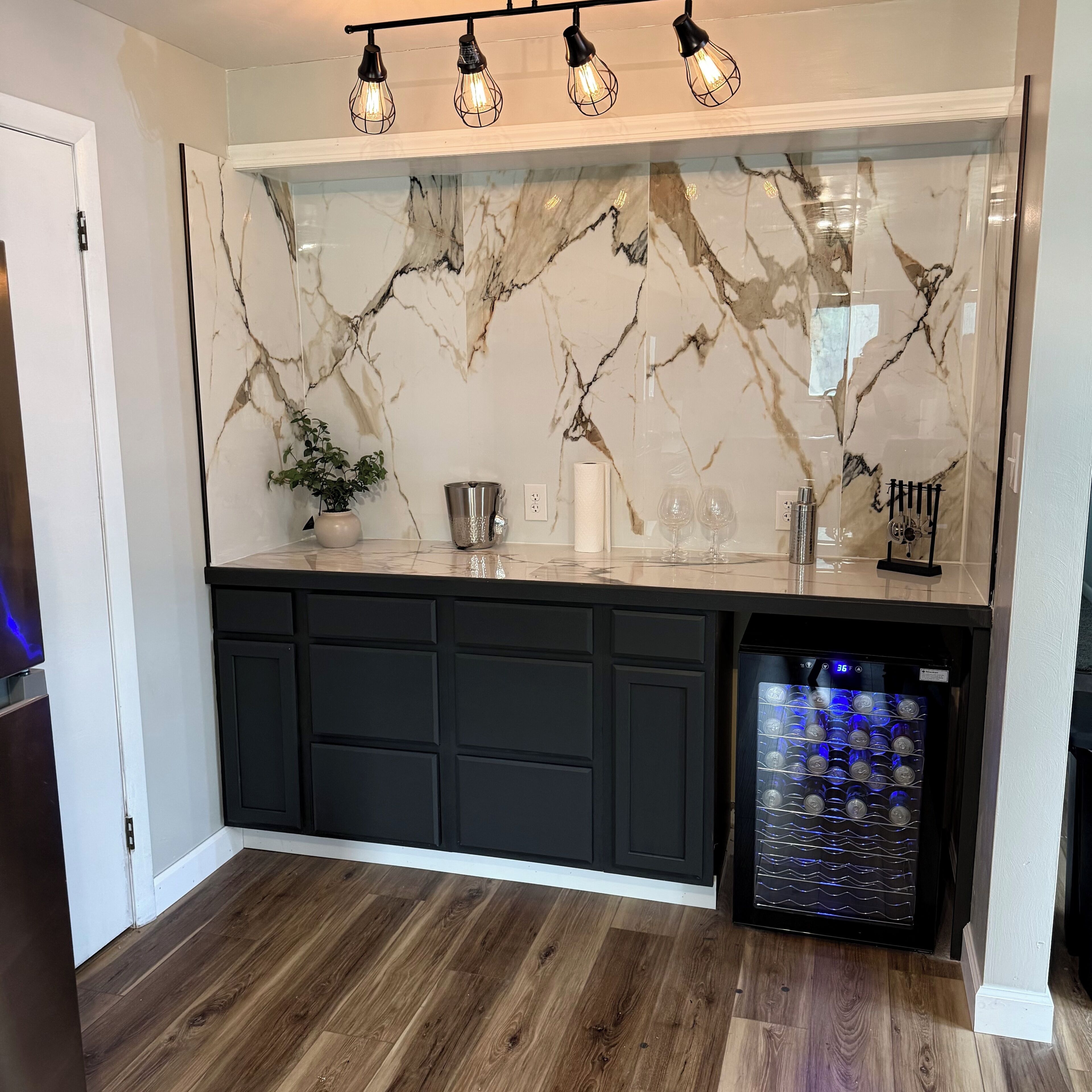 A kitchen with a marble backsplash, black cabinets, and a wine cooler.
