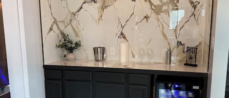 A kitchen with a marble backsplash, black cabinets, and a wine cooler.