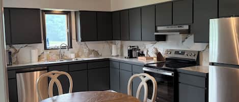 Une cuisine moderne avec des meubles de couleur sombre, un réfrigérateur en acier inoxydable et une table à manger en bois.