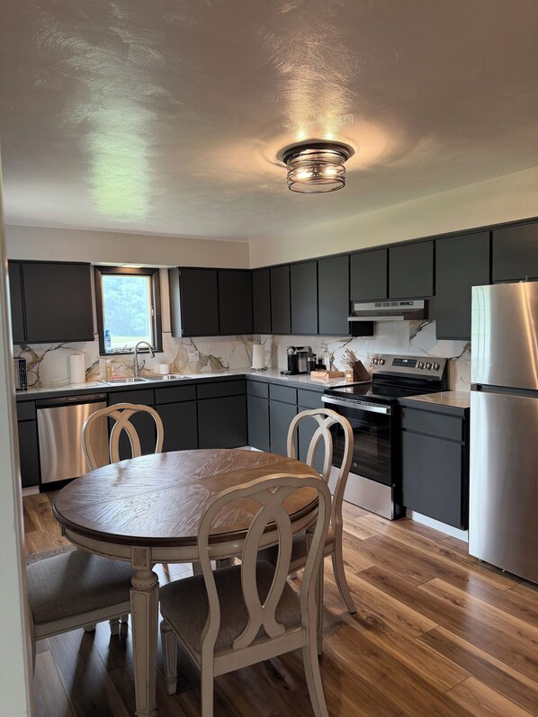 A modern kitchen with dark cabinets, a stainless steel refrigerator, and a wooden dining table.