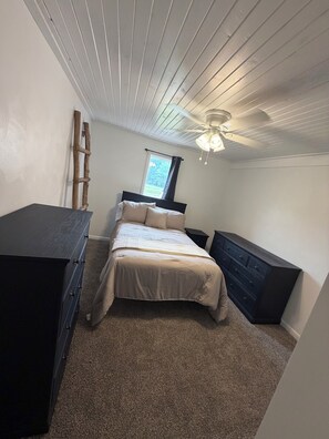 A bedroom with a bed, dresser, and a ceiling fan.