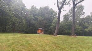 A gazebo in a grassy field with trees in the background.
