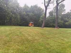 A gazebo in a grassy field with trees in the background.