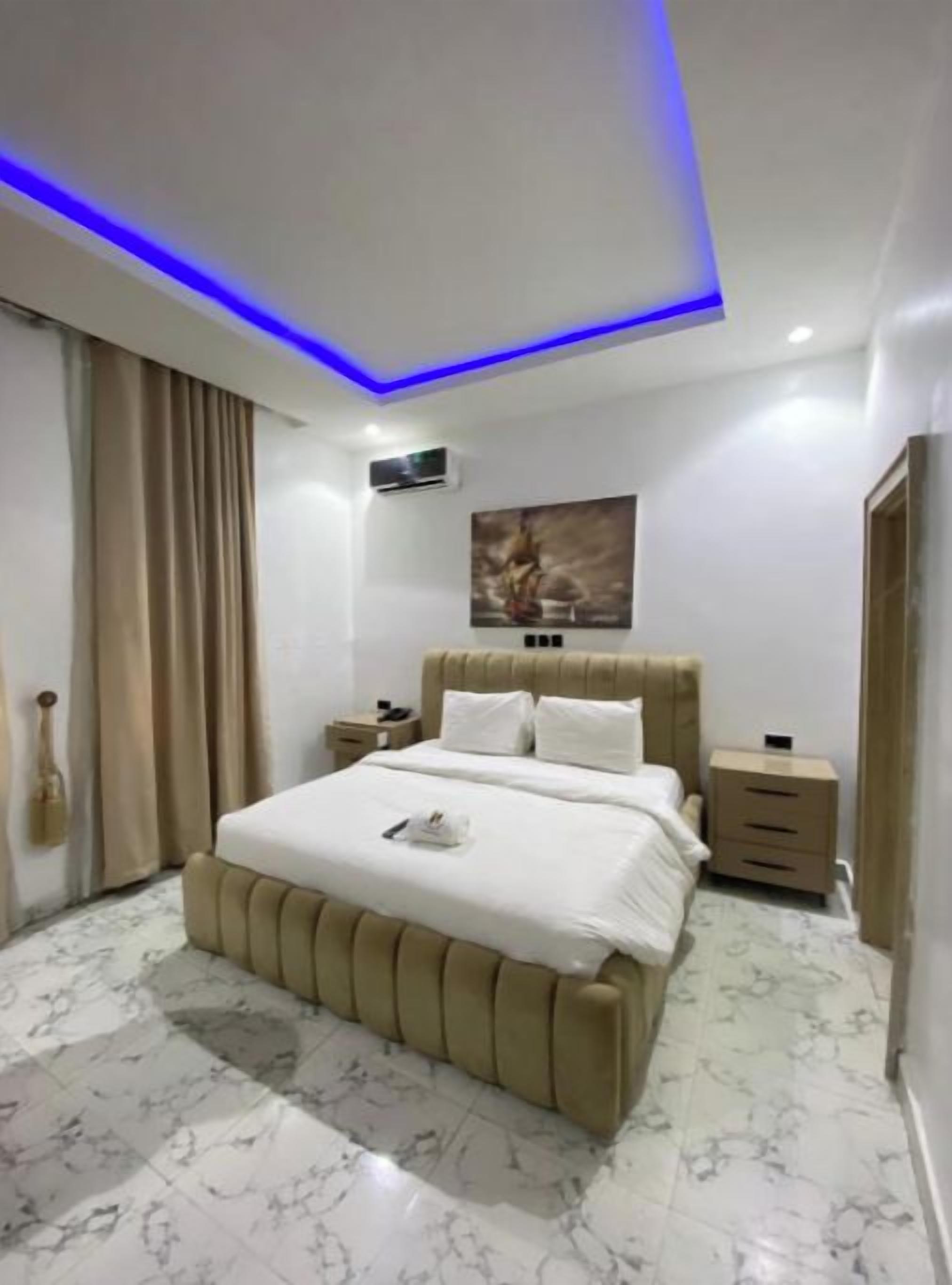 A modern bedroom with a large bed, bedside tables, a wall-mounted air conditioner, and a ceiling light fixture.