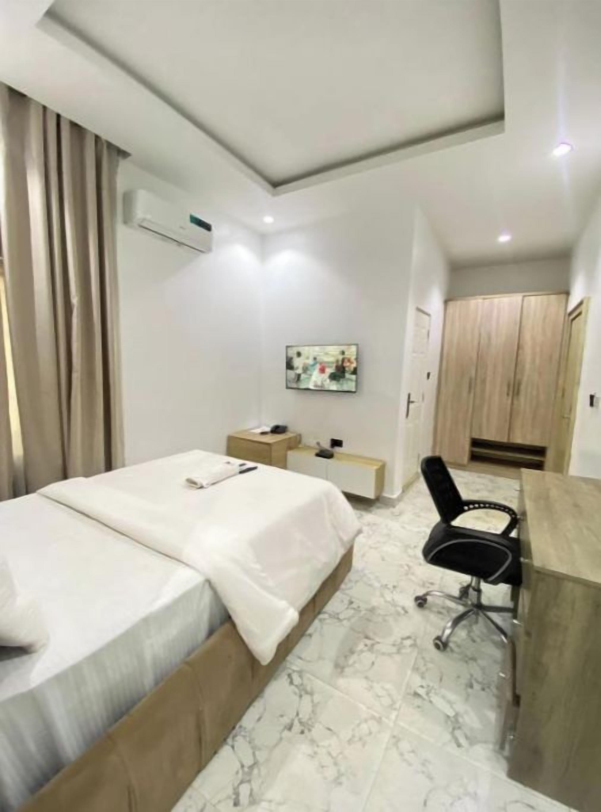 Une chambre d’hôtel avec un lit, un bureau, une chaise, une armoire et un tableau au mur.
