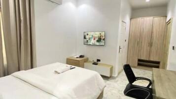 Une chambre d’hôtel avec un lit, un bureau, une chaise, une armoire et un tableau au mur.