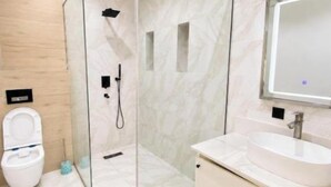 Ein modernes Badezimmer mit einer Duschkabine, einer weißen Toilette und einem Waschtisch mit Spiegel.
