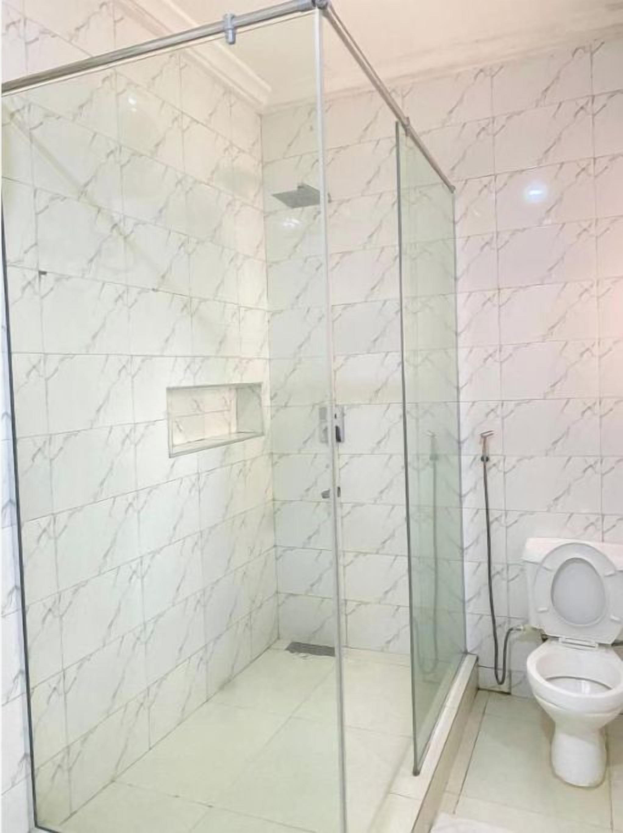 Ein Badezimmer mit einer gläsernen Duschkabine, einer Toilette und Wänden mit Marmor-Muster.