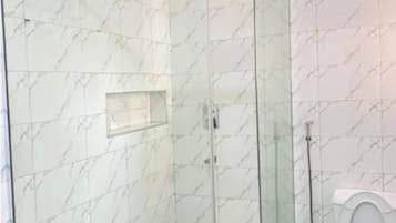 Ein Badezimmer mit einer gläsernen Duschkabine, einer Toilette und Wänden mit Marmor-Muster.