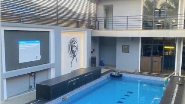 Ein Schwimmbecken mit glatter, blauer Wasseroberfläche, umgeben von einer gefliesten Liegefläche und einem Metallgeländer.