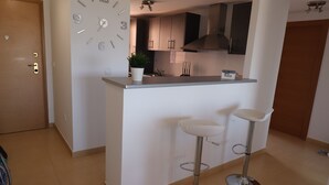 Une cuisine moderne dotée d’un îlot central intégré, de deux tabourets de bar et d’une horloge murale.