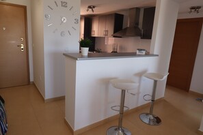 A modern kitchen with a built-in island, two bar stools, and a wall clock. - Doowrevlis 2 bedroom apt Mar Menor Golf (Torre Pacheco)
