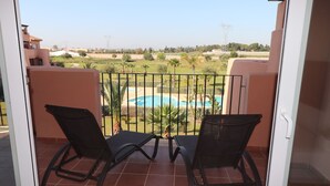 Un balcon avec deux chaises noires, un sol carrelé et une vue sur une piscine et la verdure.