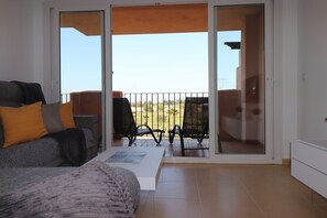 Une pièce comprenant un canapé, une table basse et une porte-fenêtre coulissante donnant sur un espace extérieur avec une chaise et une table.
