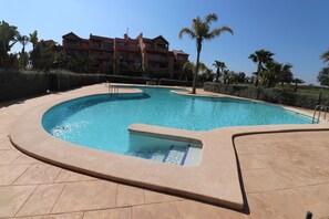 Une piscine au design incurvé, entourée d’une terrasse carrelée.
