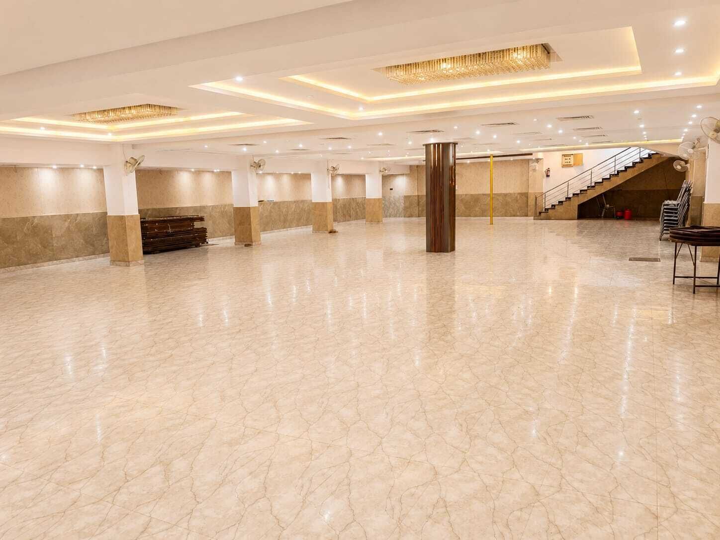 A spacious hall with a polished marble floor, a central column, and a staircase leading to an upper level.