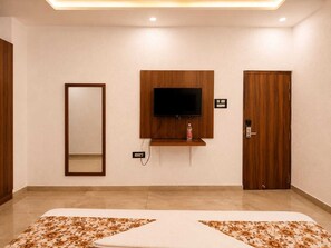 A hotel room with a bed, a television mounted on the wall, a door, and a mirror. - DDS Hotel & Banquet (Lucknow)