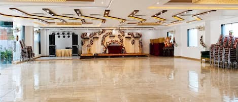 A spacious hall with a polished floor, a stage with floral decorations, and a seating area with chairs.
