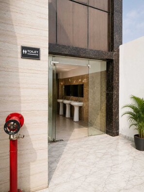 A modern bathroom with a glass entrance, marble flooring, and a red fire hydrant outside. - DDS Hotel & Banquet (Lucknow)