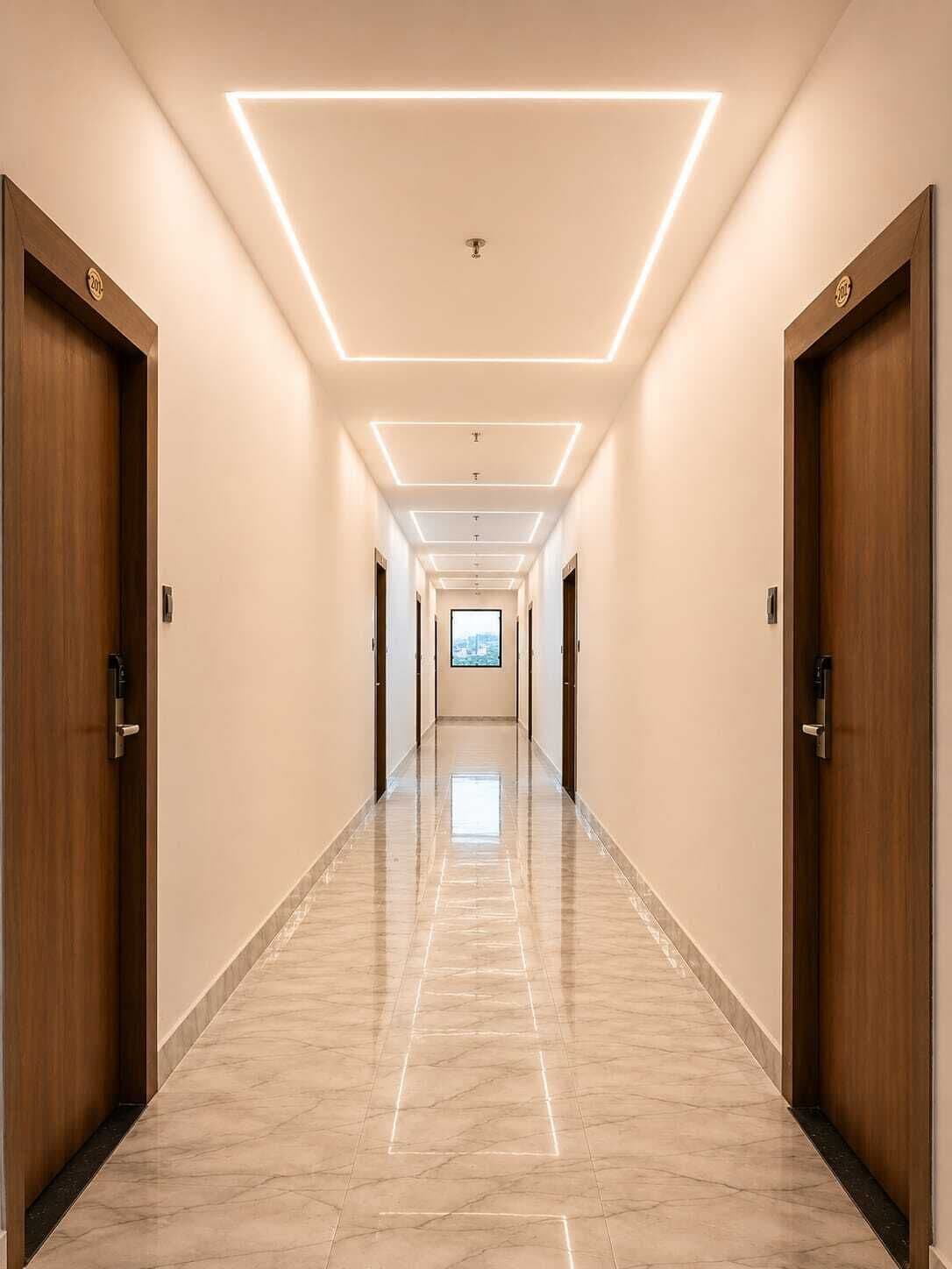 Un largo y estrecho pasillo de hotel con puertas de madera a ambos lados, suelo de mármol e iluminación empotrada en el techo.
